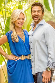 a man and woman standing next to each other in front of green plants, smiling at the camera