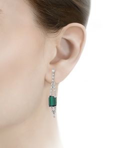 a close up of a woman's ear wearing earrings with green stones and diamonds