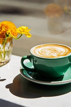 a cup of cappuccino on a saucer next to a vase with yellow flowers