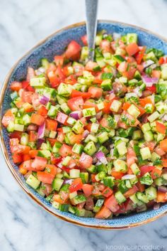 a blue bowl filled with cucumber, tomato and onion salad on top of a marble counter