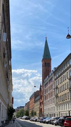 a city street with cars parked on both sides and a clock tower in the background