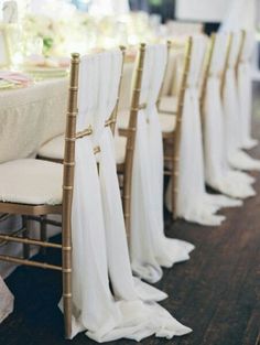 a row of chairs with white drapes draped over them at a table set for an event