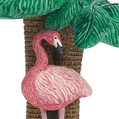 a pink flamingo standing next to a palm tree and a basket with leaves on it