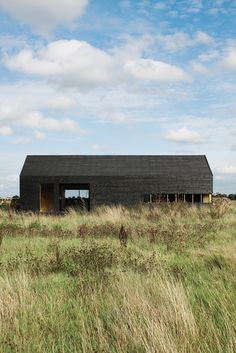 a black house sitting on top of a lush green field next to a tall grass covered field