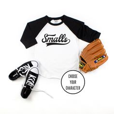 a baseball glove and ball mitt are sitting on the floor next to a t - shirt that says smalls