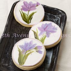 three decorated cookies with flowers on them sitting on a black platter next to a white tablecloth