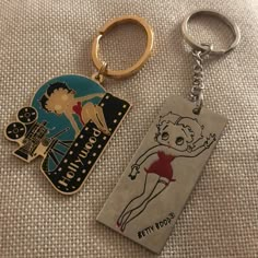 two key chains that are on top of a cloth covered surface, one has a pin and the other has an image of a woman