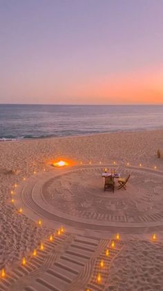 candles are arranged in the shape of a circle on a sandy beach near the ocean