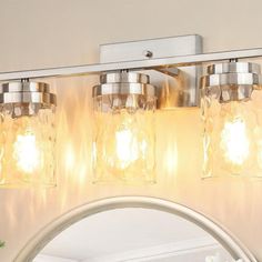 a bathroom vanity light with three jars on the top and one in the bottom, above a mirror