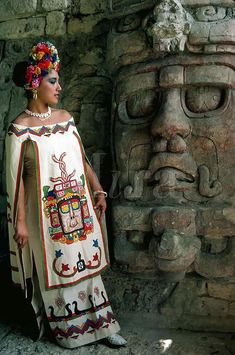 a woman standing next to a stone statue wearing a white dress and headdress