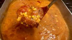 a spoonful of soup with corn on the cob and meat in tomato sauce