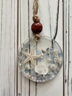 a glass ornament with shells and starfish hanging on a white wooden wall