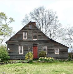 an old wooden house with a red door and window on the front lawn, surrounded by trees