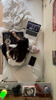 a woman laying in bed with her laptop and headphones on top of her desk