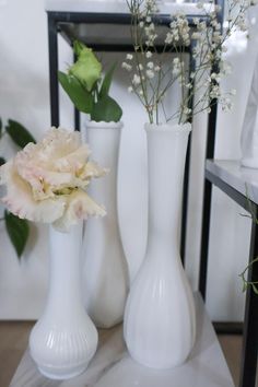 three white vases with flowers in them on a table