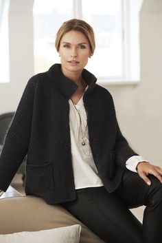 a woman sitting on top of a couch wearing a black jacket and white shirt with her hands in her pockets