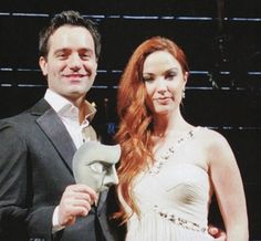 a man and woman standing next to each other in front of a stage backdrop holding an award