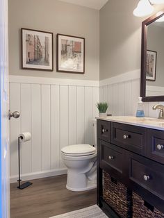 a white toilet sitting in a bathroom next to a wooden sink vanity with two framed pictures on the wall