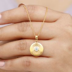 a woman's hand holding a gold necklace with a diamond in the center and a round pendant attached to it