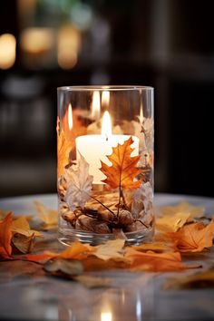 a candle that is sitting in some glass with leaves on the table next to it