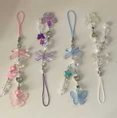 four different colored butterfly lanyards on a white surface with beads and charms hanging from them