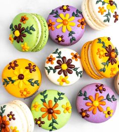 colorful decorated macaroons are arranged on a white surface, including one with flowers