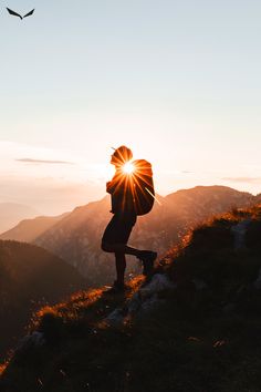 a person standing on top of a hill with the sun setting behind them and birds flying overhead