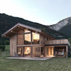 a large wooden house sitting in the middle of a lush green field next to mountains