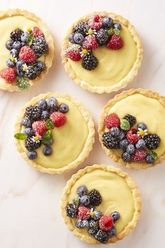 four small pies topped with fresh fruit on top of a white countertop next to each other