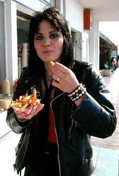 a woman in black jacket eating food on sidewalk