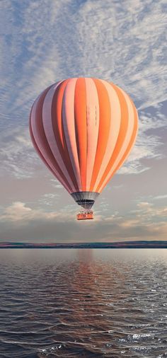 an orange and white hot air balloon flying over the ocean