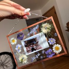 a person holding up a small frame with flowers on it and a chain hanging from the side