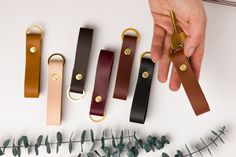 four leather key fobs in different colors and sizes, one being held by a person's hand