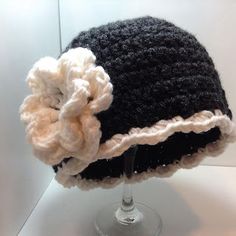 a crocheted hat with a flower on it sitting on top of a glass stand