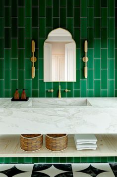 a bathroom with green tiles and white counter tops, gold fixtures and wooden utensils