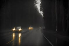 two cars driving down the road in the rain at night with headlights shining on them