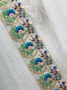 a blue and green floral embroidered ribbon on white wooden background with gold trimmings