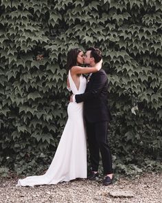 a bride and groom kissing in front of a wall covered with green ivys at their wedding