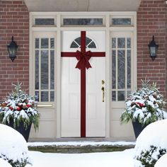 a white door with a red ribbon on it and two potted plants in front