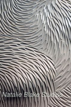 an artistic metal surface with wavy lines and curves in grey tones, as well as the words nattie bake studios