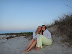 two women are sitting on the sand at sunset