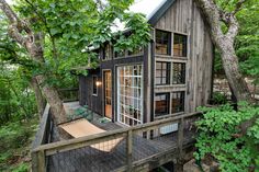 a small wooden cabin in the woods with a hammock hanging from it's side