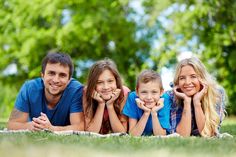 a family laying on the grass with their hands under their chins and smiling at the camera