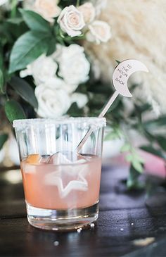 a glass filled with liquid sitting on top of a wooden table next to white flowers