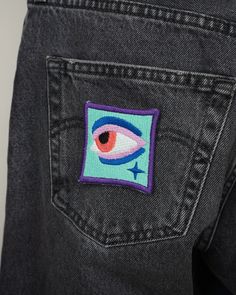 the back pocket of a pair of jeans with an embroidered eye patch on one side