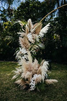 an arrangement of white and brown flowers in the middle of a grass field with trees in the background