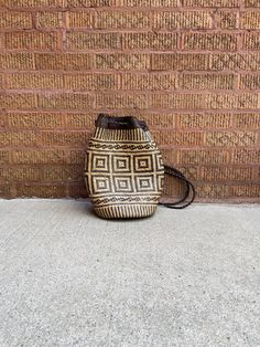 a brown and white basket sitting on the ground next to a brick wall with a black handle