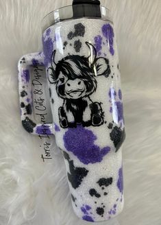 a purple and white coffee mug with a cow on it's side sitting on a furry surface