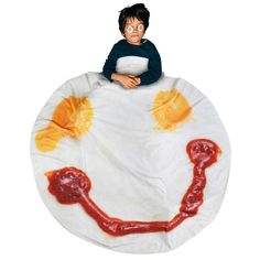 a woman sitting on top of a giant pillow covered in ketchup and mustard