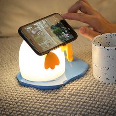 a penguin lamp with a cell phone in it's hand next to a cup